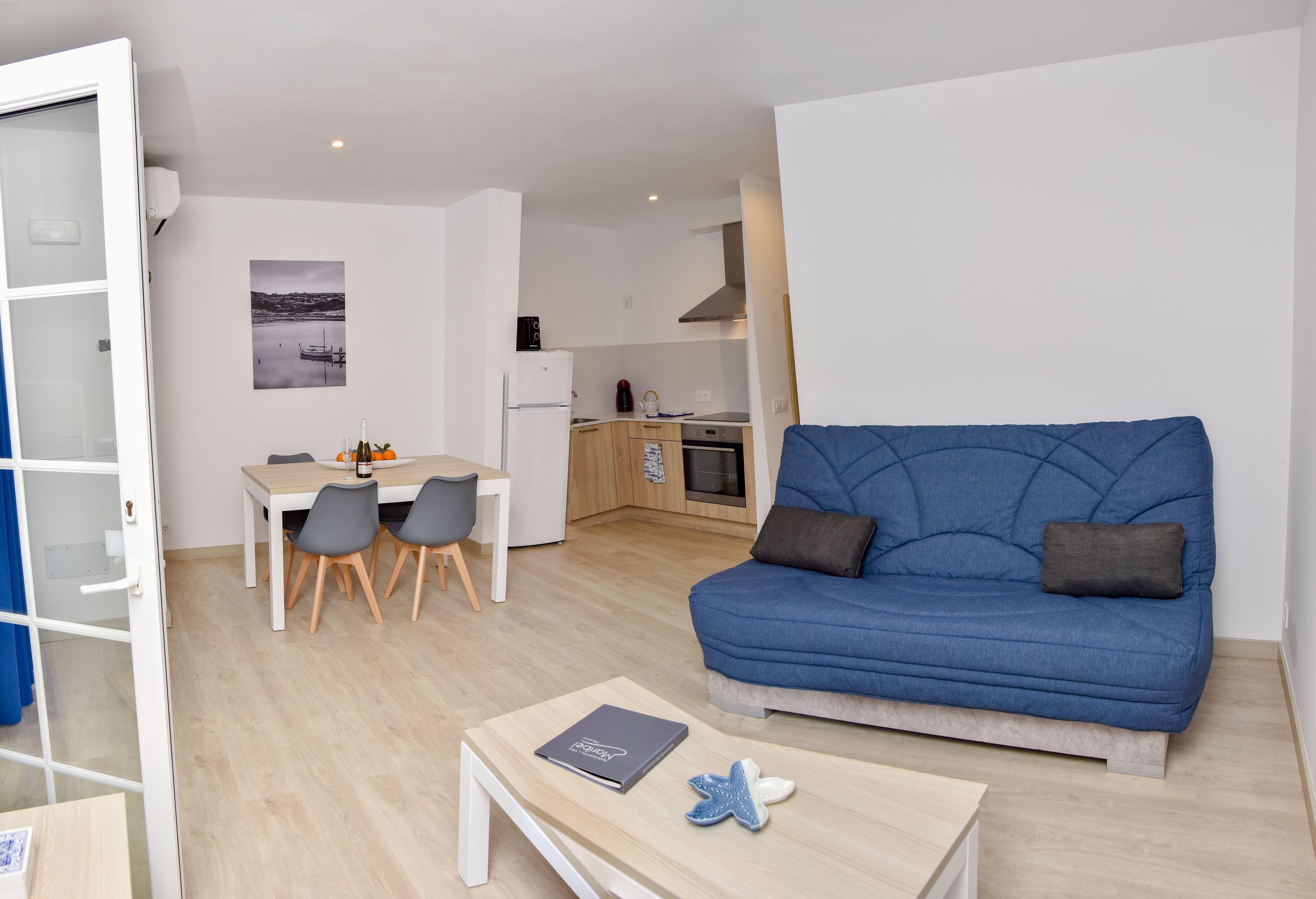 A modern living room with a blue sofa, a dining table with chairs, and a kitchen in the background.