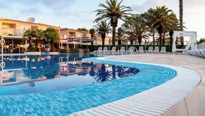 Ein Swimmingpool mit Liegestühlen und Sonnenschirmen, umgeben von Gebäuden und Palmen.