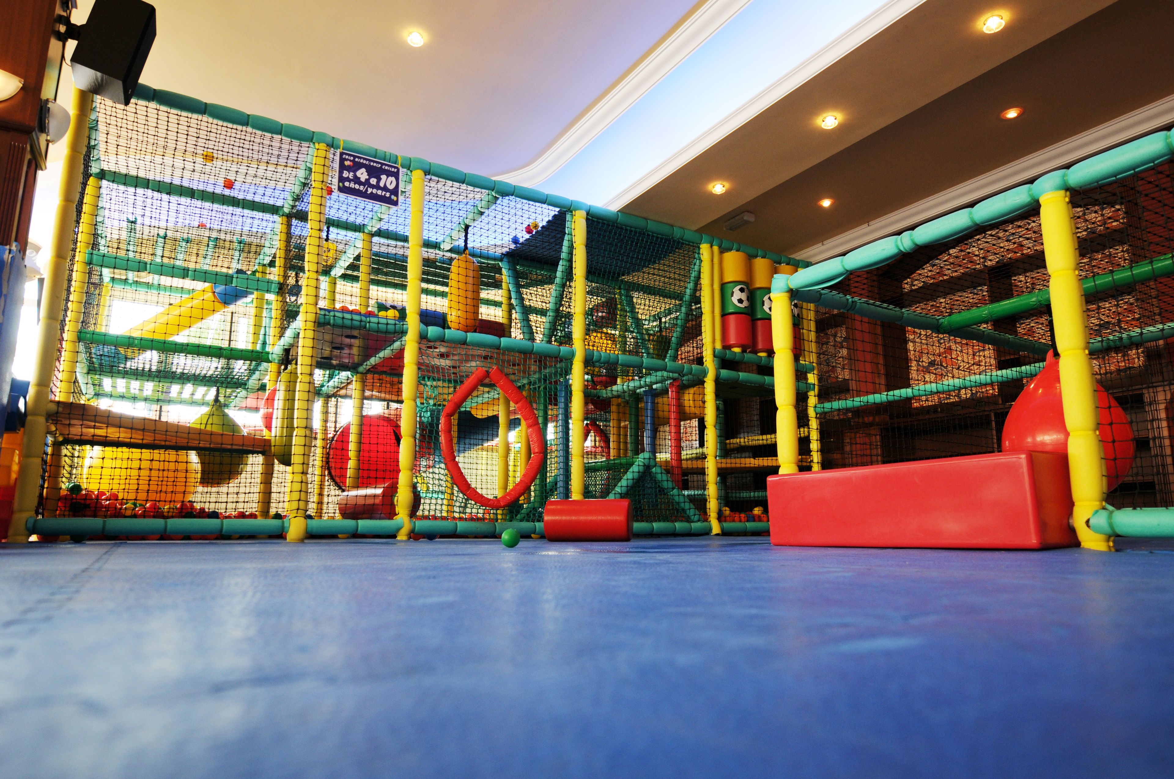 Un área de juegos interior con estructuras de escalada cubiertas por red y superficies de juego acolchadas.
