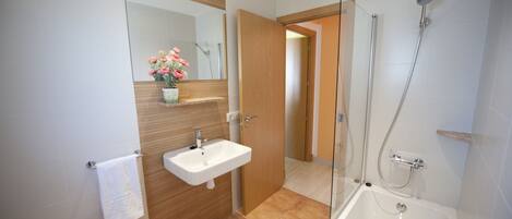 A modern bathroom with a white sink, a glass-enclosed shower, and a wooden vanity.