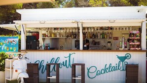 Eine weiße Außenbar namens 'Chillout Cocktail Bar' mit einer Theke, auf der verschiedene Flaschen und Snacks präsentiert werden.