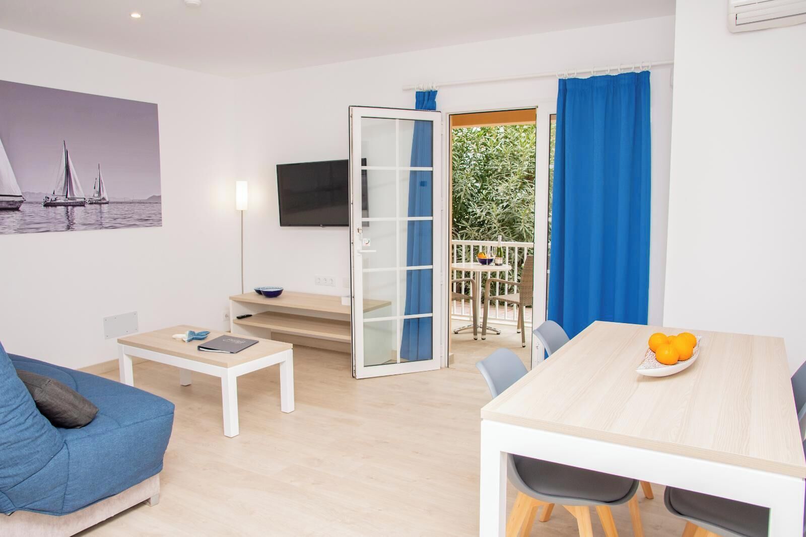 Un salon moderne avec un canapé, une table basse, un téléviseur et un balcon agrémenté de rideaux bleus.