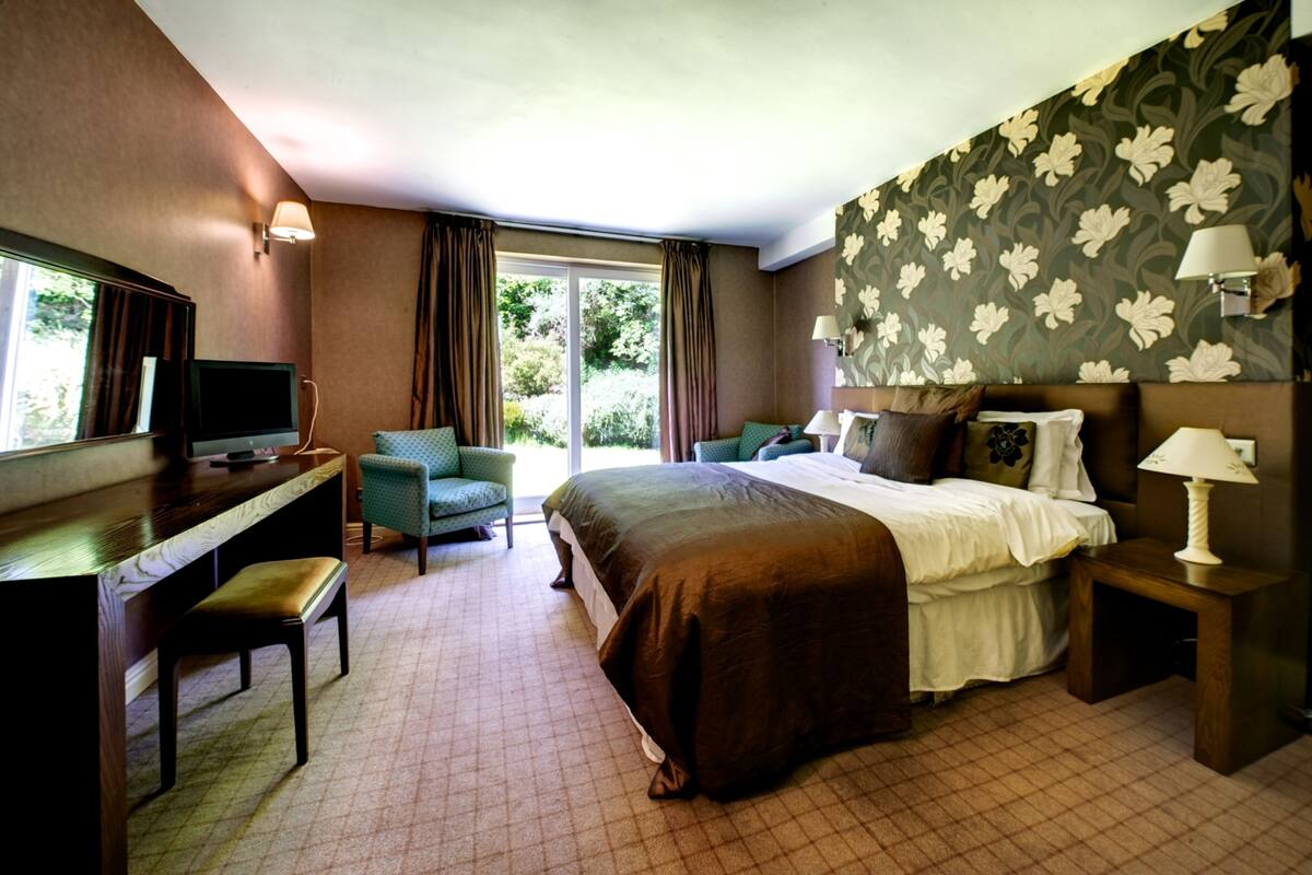 A hotel room with a bed, a desk, a chair, a TV, and a window with curtains.