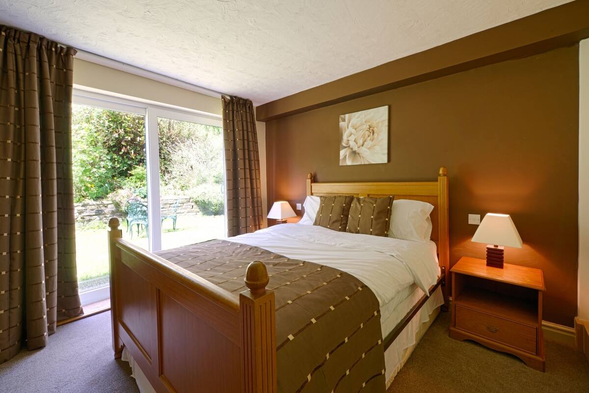 A bedroom with a large bed, two bedside tables with lamps, a window with curtains, and a painting on the wall.