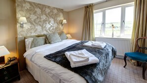 Een hotelkamer met een groot bed, twee bedlampen, een nachtkastje met een telefoon, een stoel en een raam met gordijnen.