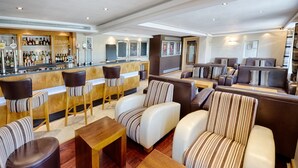 Een bar met krukken en een toonbank, een zithoek met banken en stoelen, en een bar gevuld met flessen.