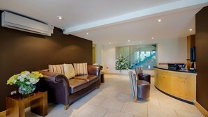 Een moderne lobby met een leren bank, een houten bijzettafeltje met bloemen, een receptiebalie en een trap op de achtergrond.