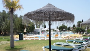 Un área junto a la piscina con sillones de descanso y sombrillas.