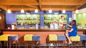 Zona de bar con techo de madera, varios taburetes y un bartender atendiendo a un cliente.
