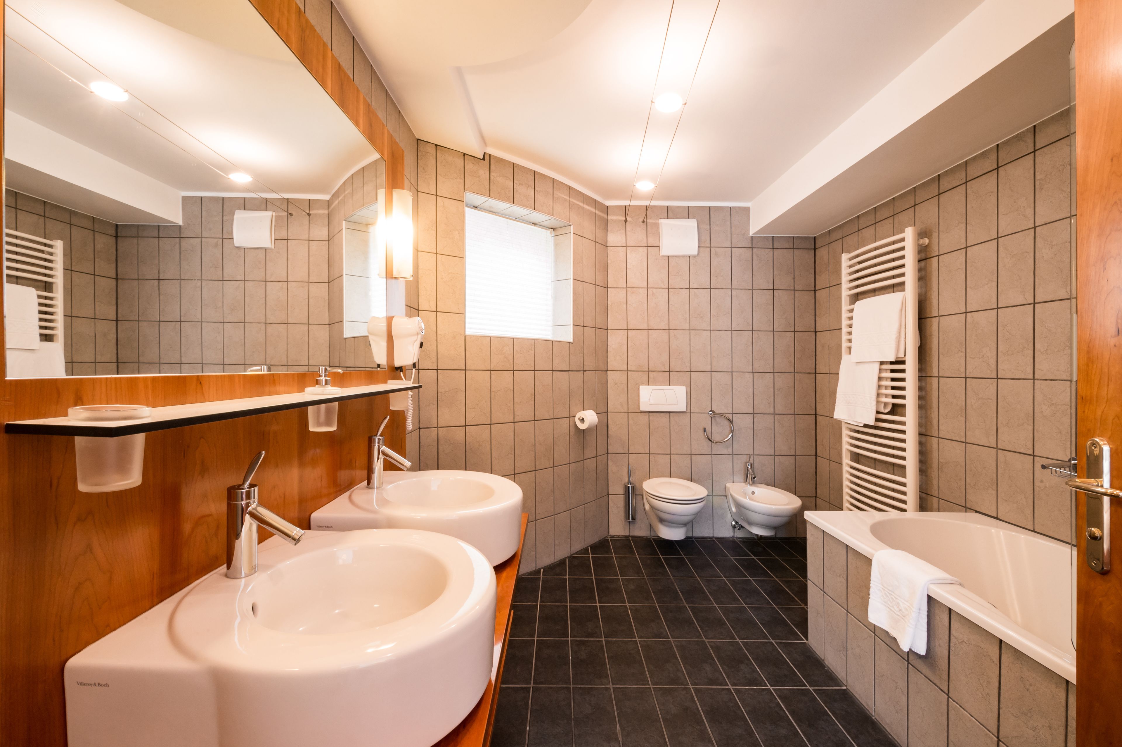 Et moderne badeværelse med to håndvaske, toilet, bidet og et badekar.