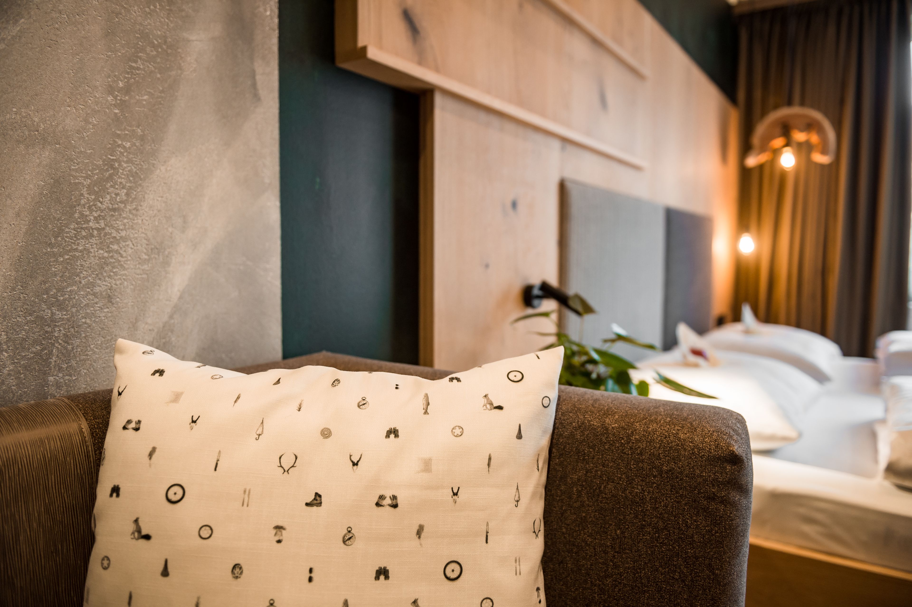 A hotel room with a brown sofa, a patterned pillow, a bed with white linens, and a wooden headboard.