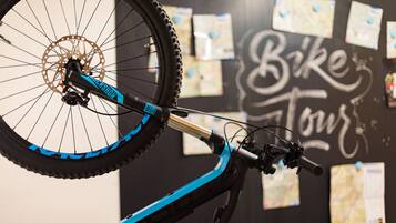 Una bicicletta con freno a disco e telaio blu, posizionata di fronte a un muro con un cartello 'Bike Tour' e mappe affisse.
