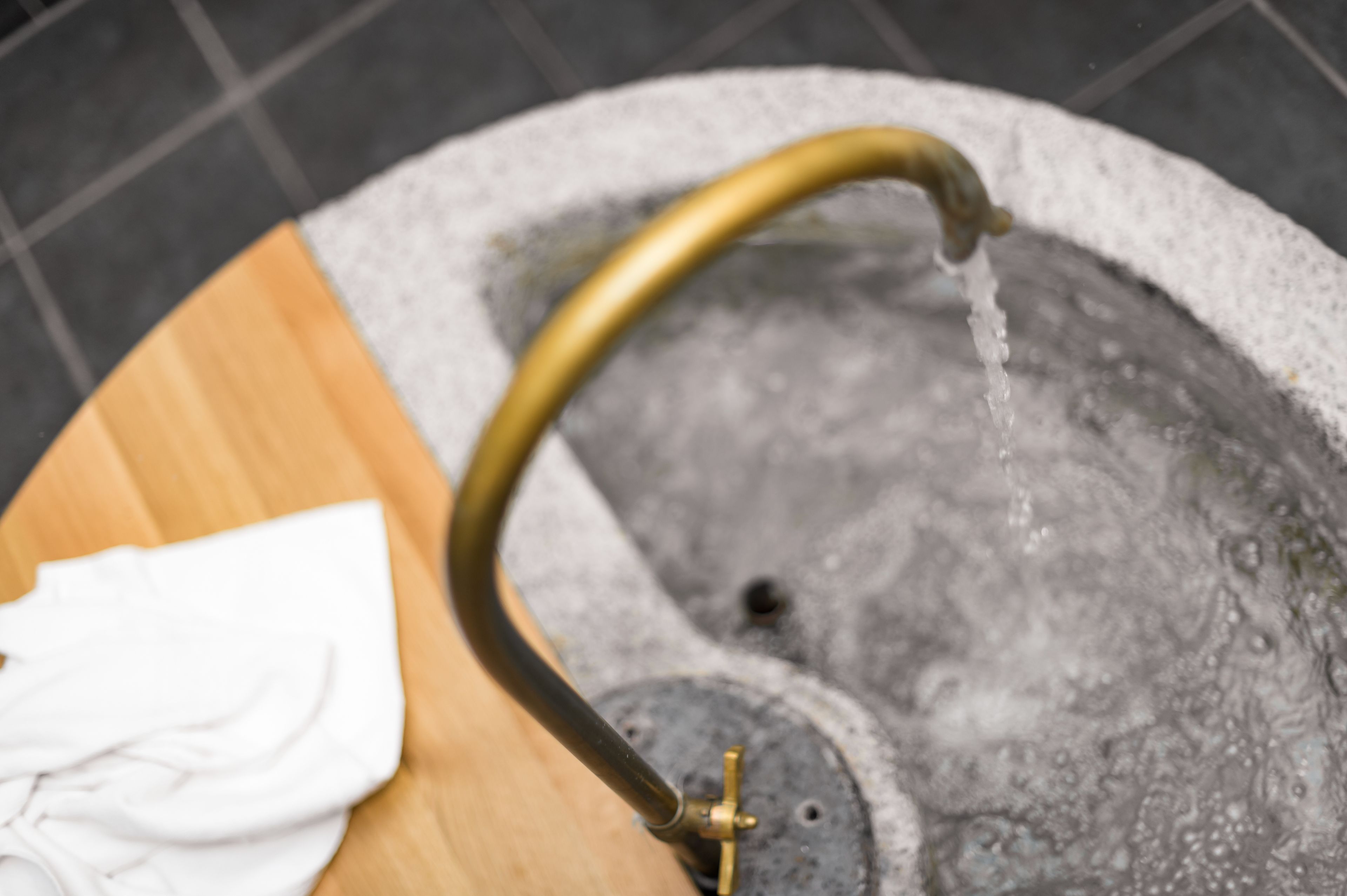 A close-up of a stone basin with a brass faucet, a white cloth, and a wooden surface.