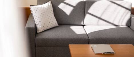 A modern living room with a grey sofa, a wooden coffee table, and a patterned pillow.