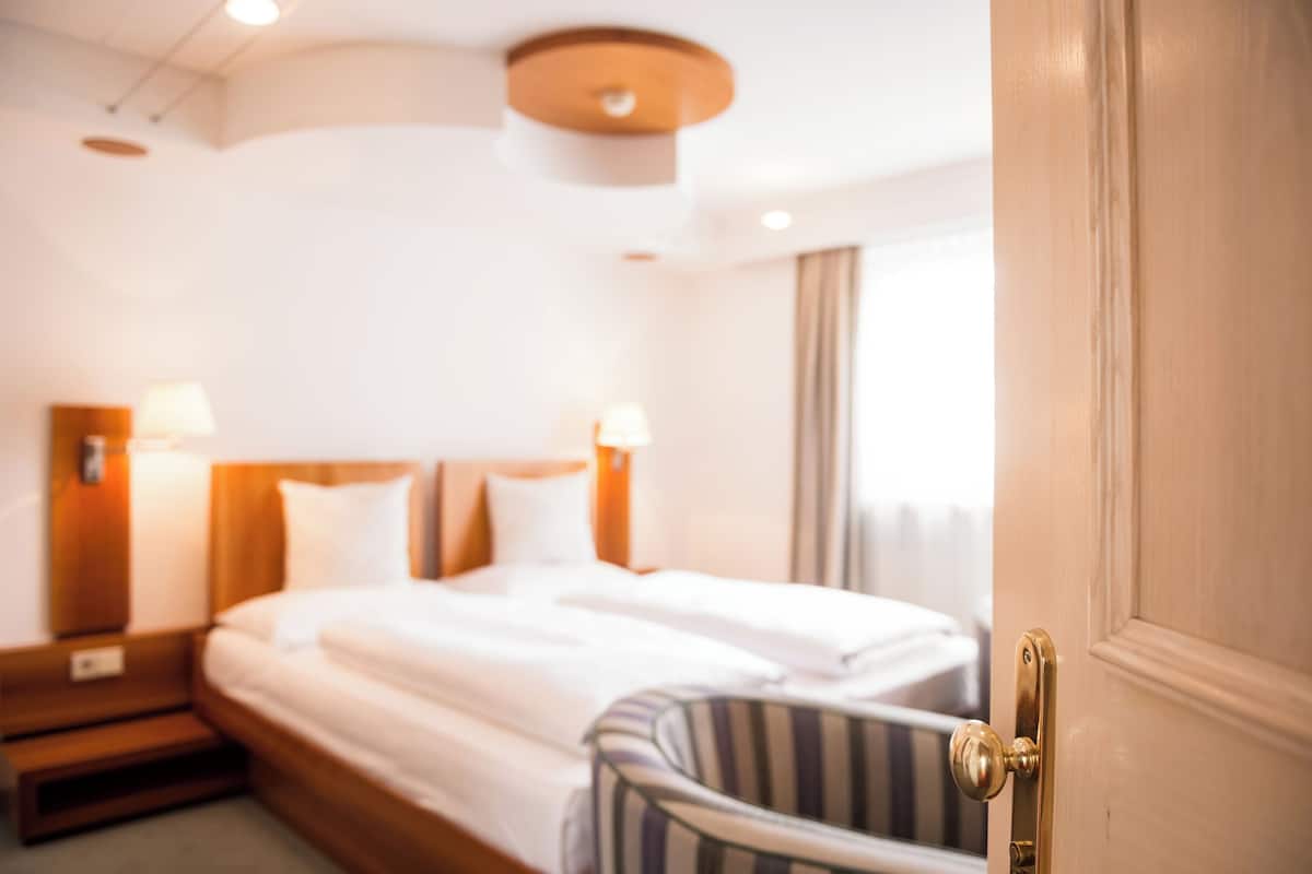 A hotel room with a bed, bedside lamps, a wooden headboard, and a door with a brass handle.