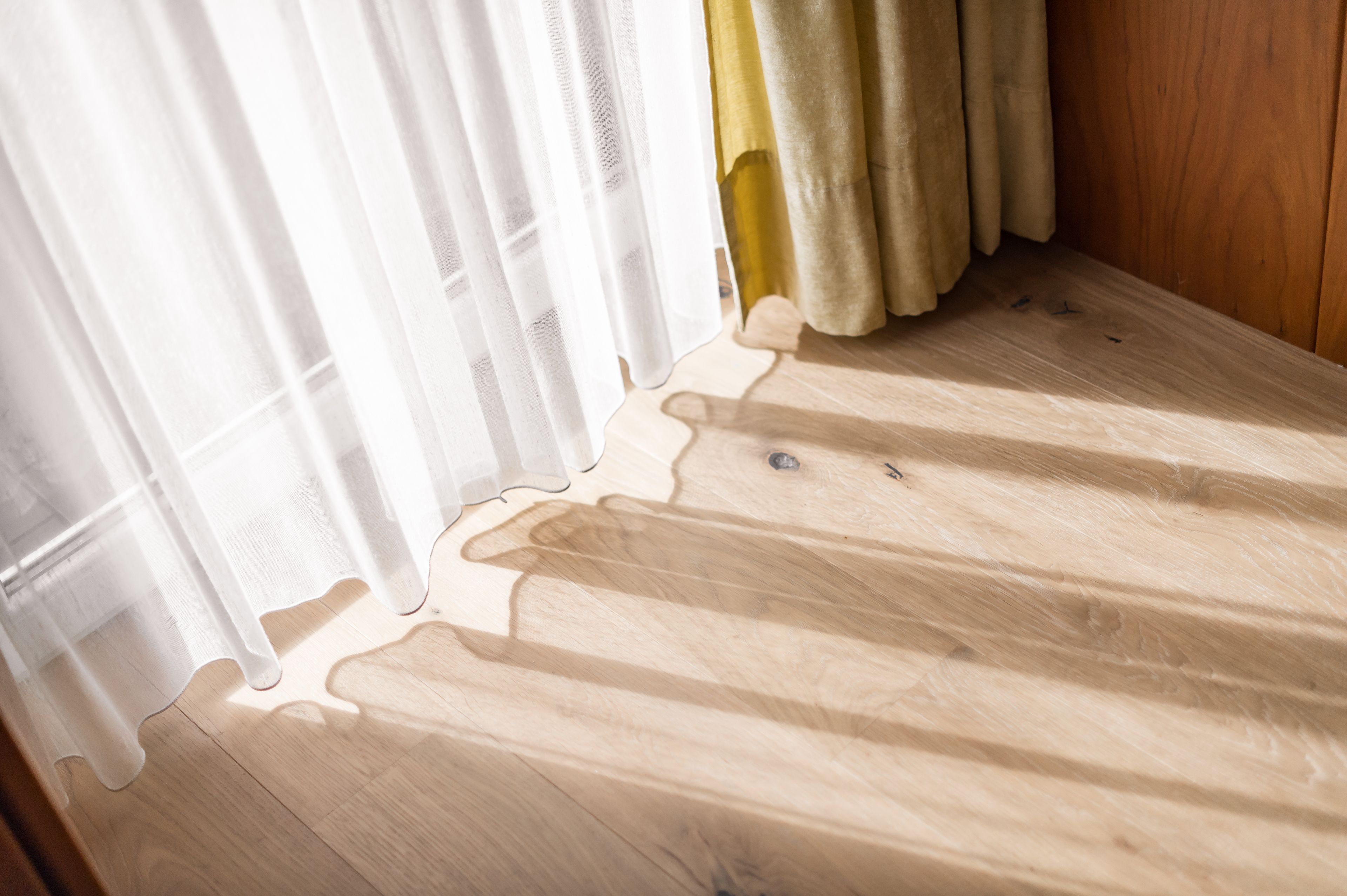 A wooden floor with a light-colored rug, white curtains, and a yellow curtain partially visible.