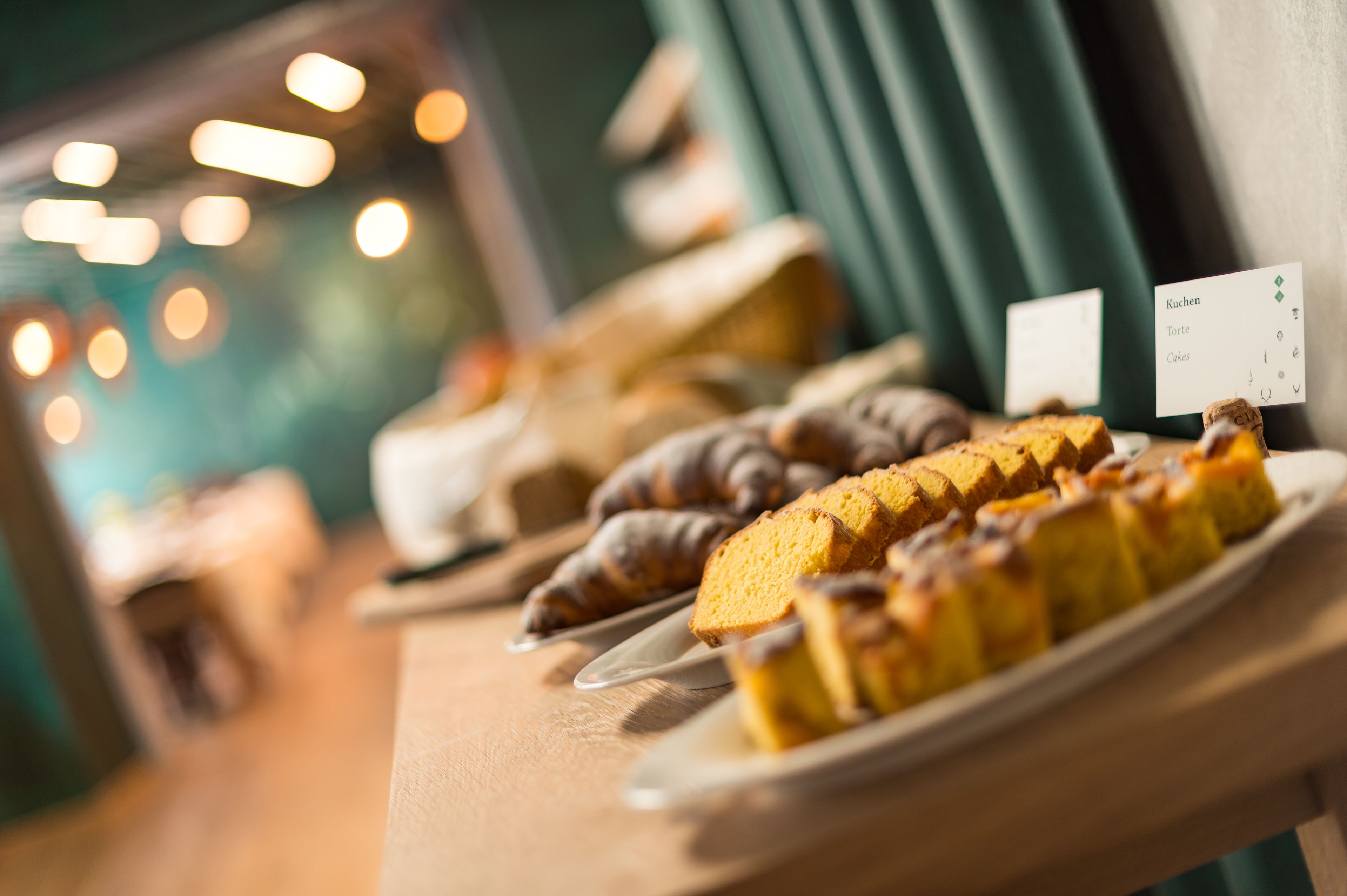 Una presentación de postres con varios pasteles y productos de pastelería en platos, con una tarjeta de menú visible al fondo.