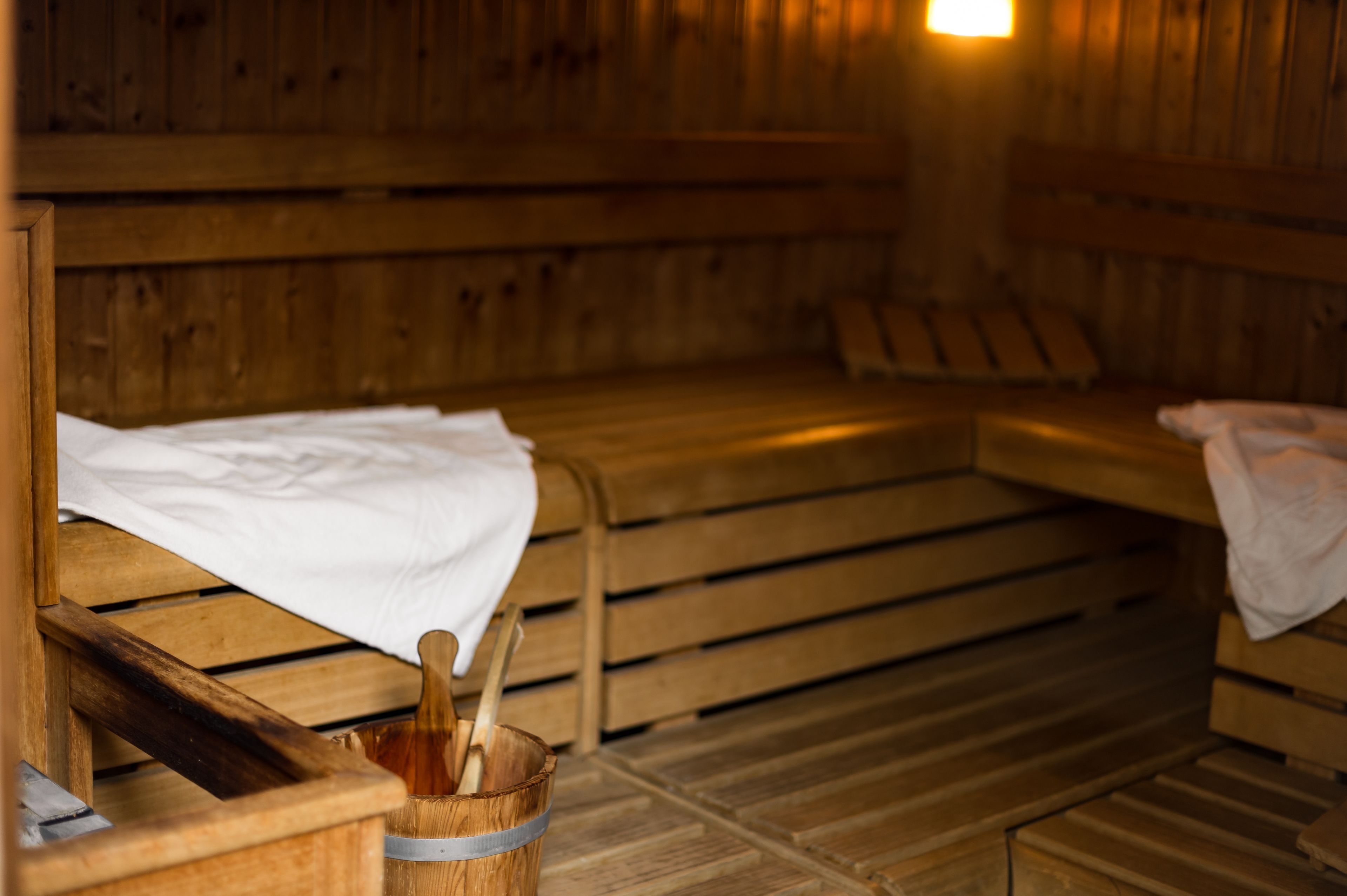 Un sauna avec des bancs en bois, un seau en bois contenant une serviette et un banc muni d’une serviette.