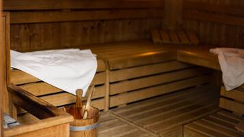 Un sauna avec des bancs en bois, un seau en bois contenant une serviette et un banc muni d’une serviette.