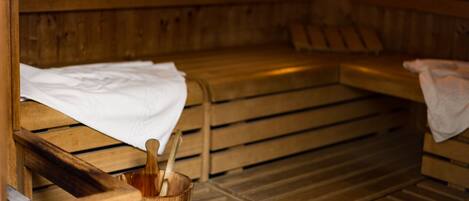 Un sauna avec des bancs en bois, un seau en bois contenant une serviette et un banc muni d’une serviette.