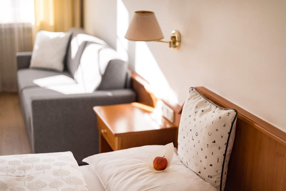 A hotel room with a bed, a nightstand, a lamp, and a sofa.