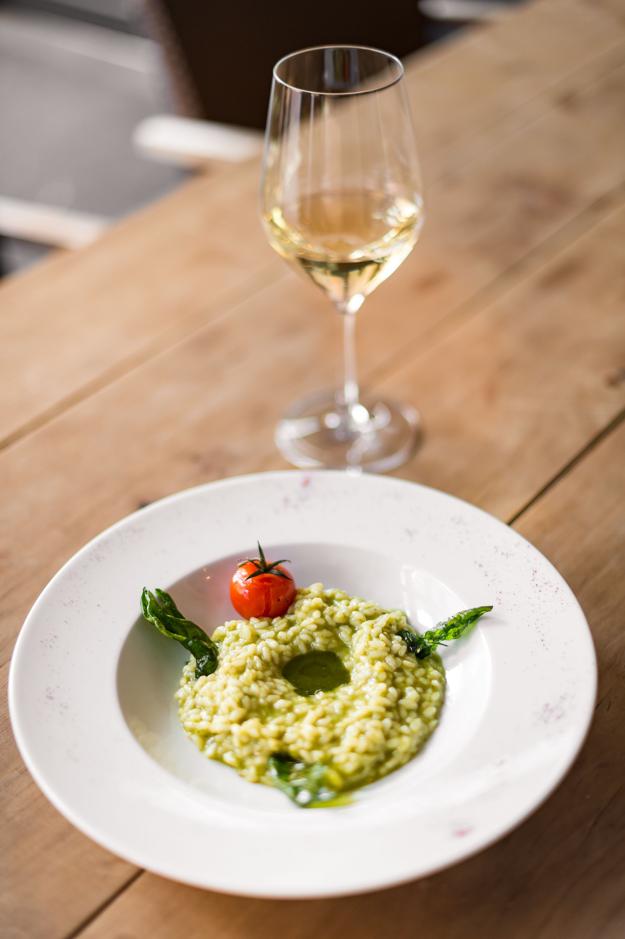 Un plato de comida con una copa de vino blanco sobre una mesa de madera.
