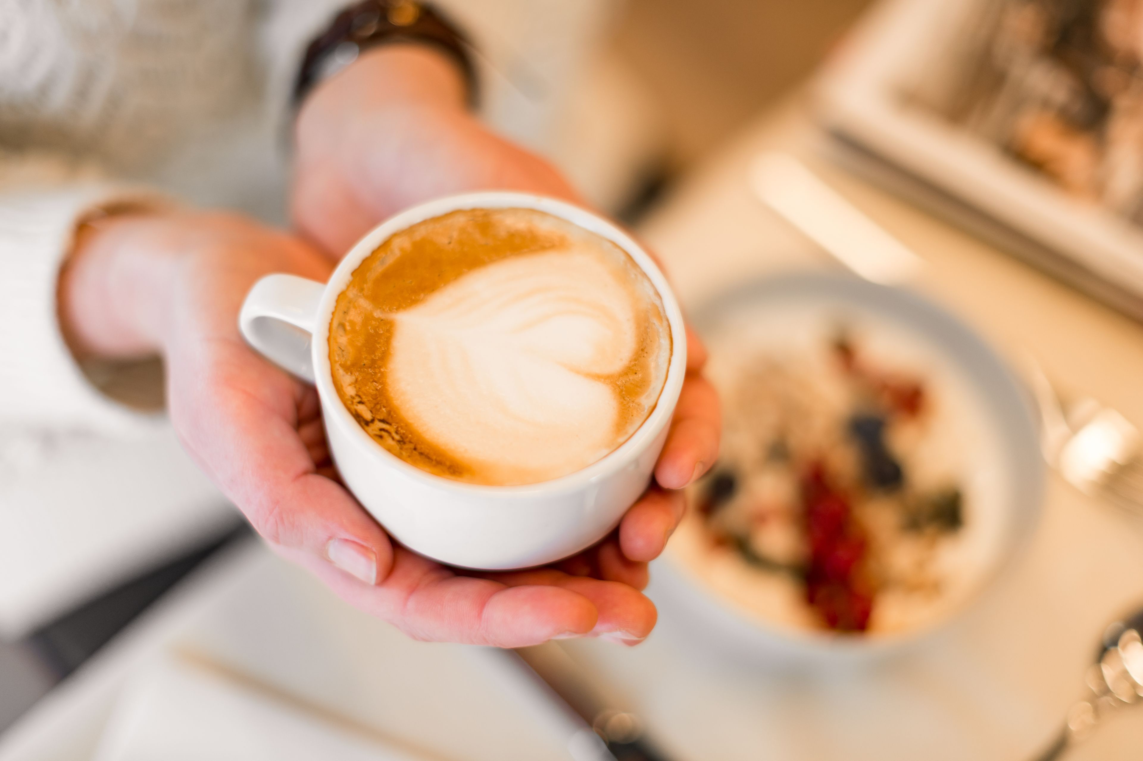 A person holding a cup of coffee with a heart-shaped latte art.