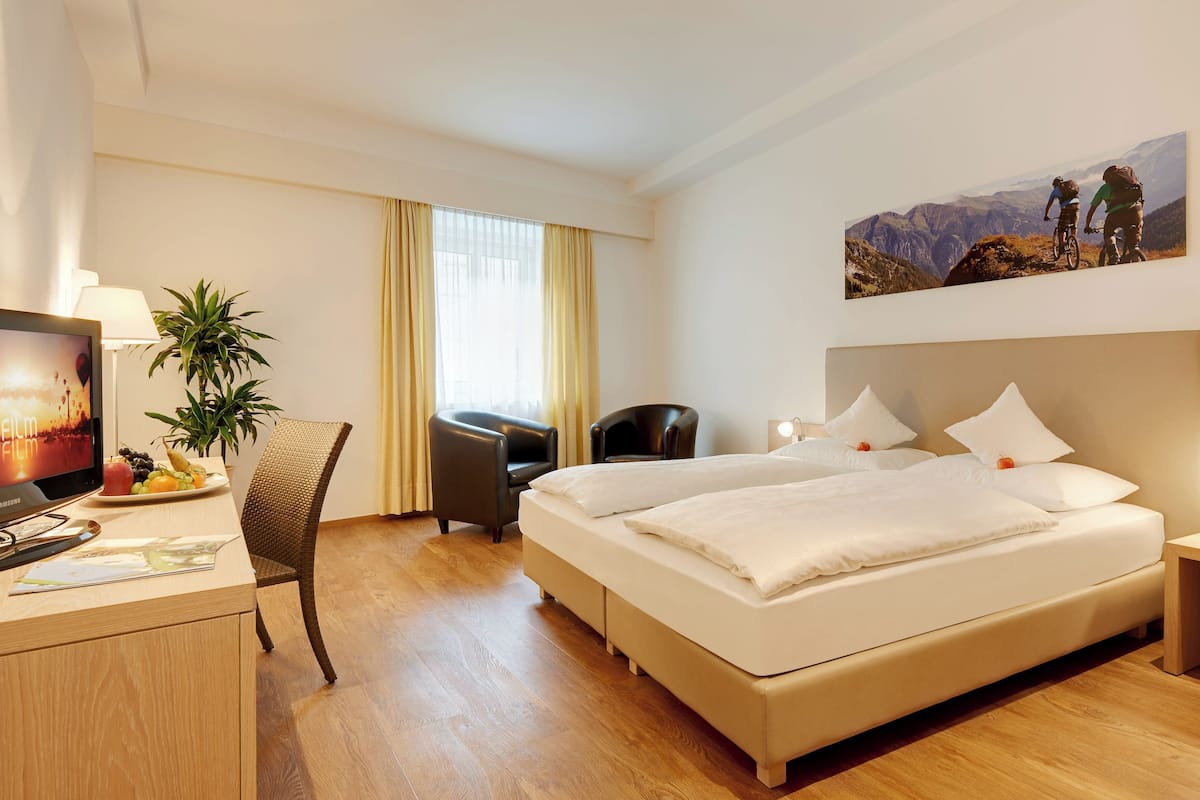 A hotel room with a bed, desk, chair, TV, and a painting on the wall.