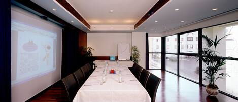 A conference room with a long table, chairs, a projector screen, and a whiteboard.