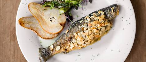 A white plate with a fish, potato slices, and greens on a wooden table.