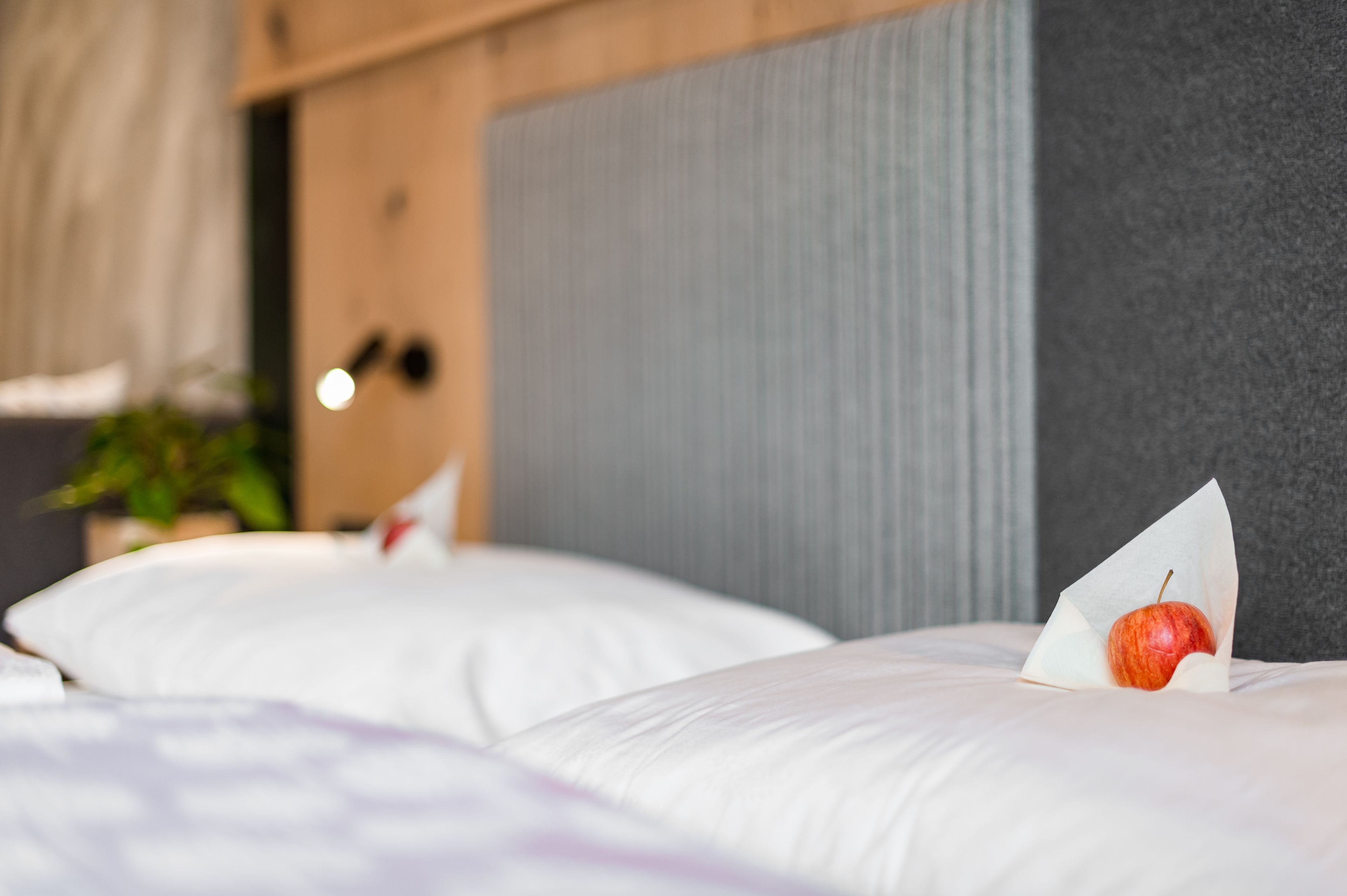 A hotel room with a bed, pillows, and a decorative apple on the bed.