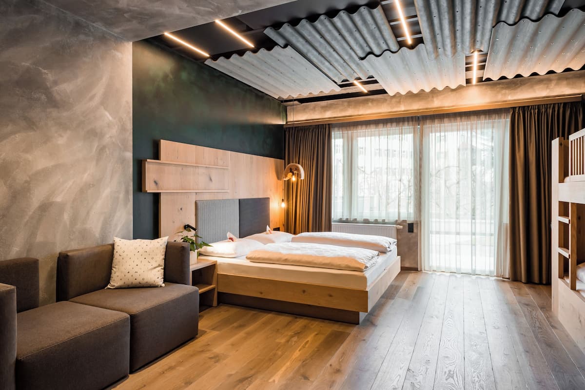 A modern bedroom with a wooden bed, a sofa, and a large window with curtains.