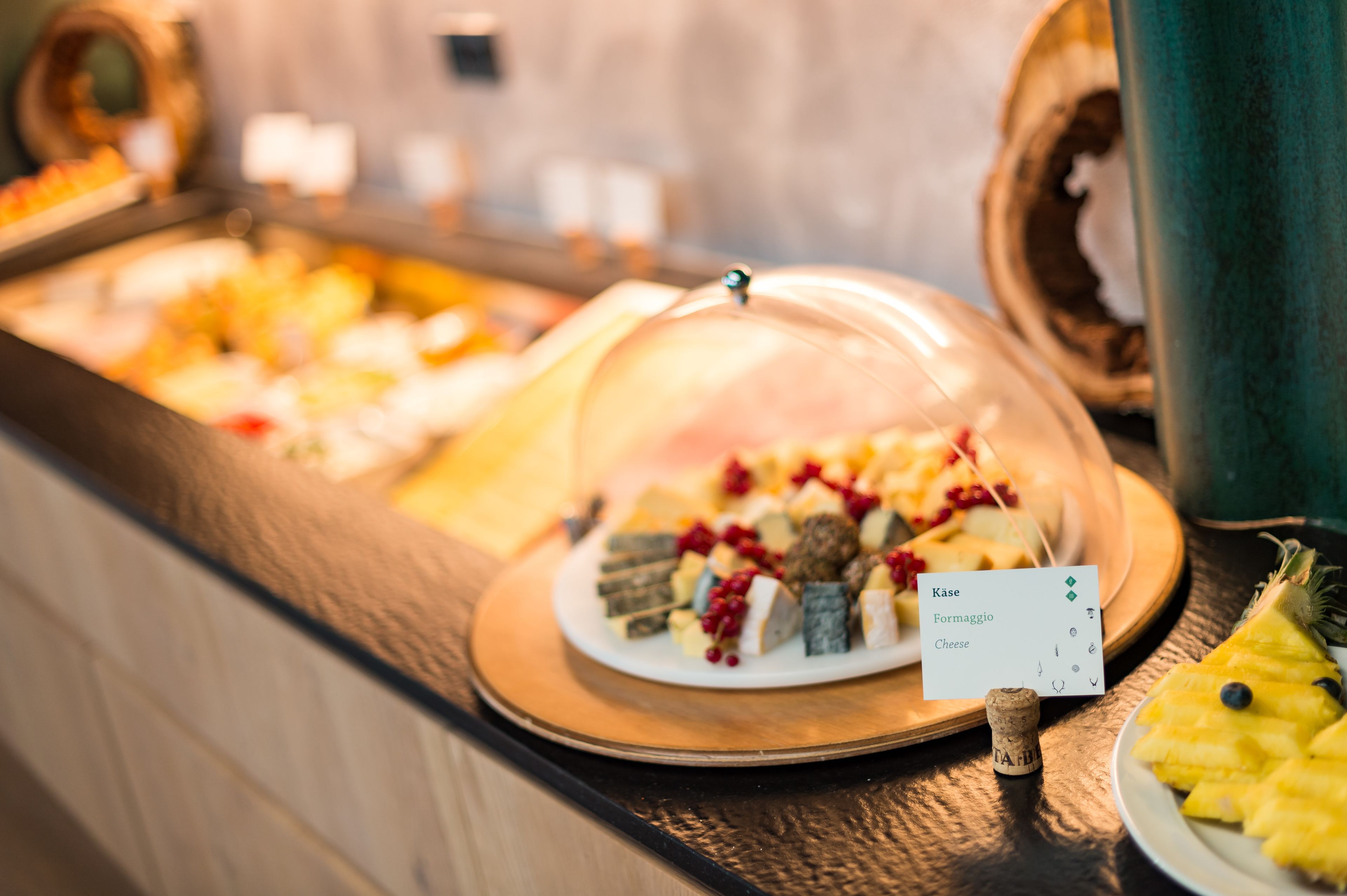 Un bufé con diversos alimentos, entre ellos queso y frutas, bajo una cúpula de vidrio.
