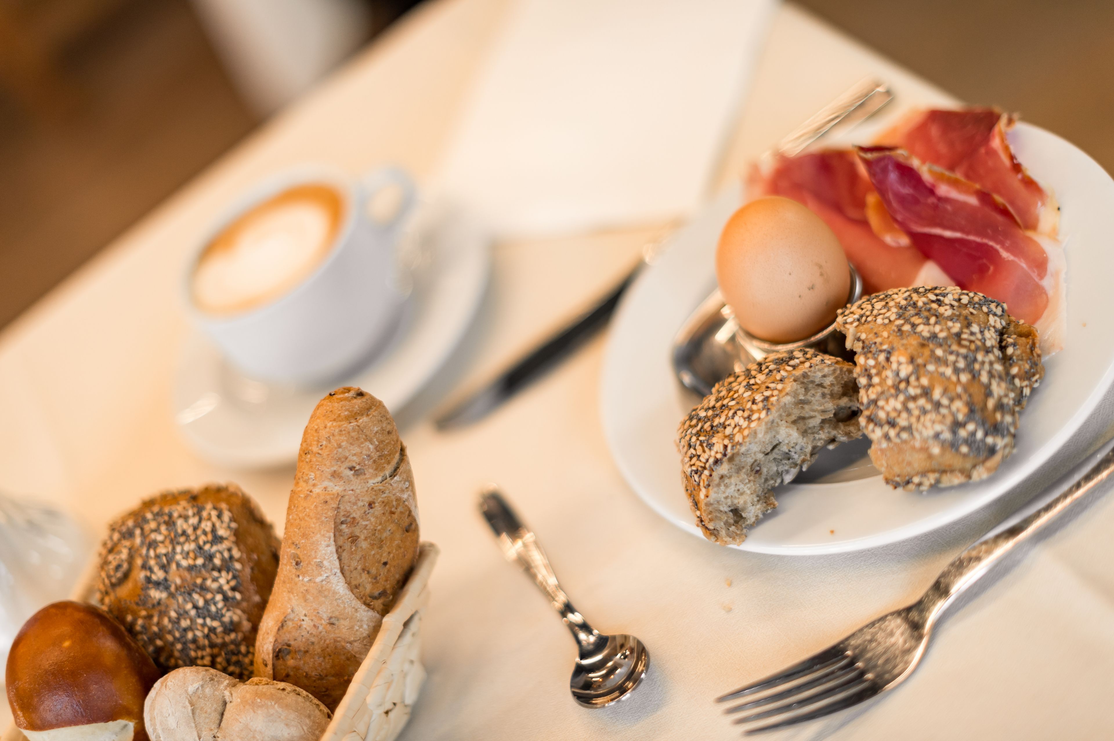 Een ontbijttafel met brood, eieren en vlees op een bord, een kop koffie en bestek.