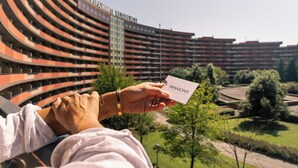 A person holding a card with "RIPAMONTI" text, standing in front of a large, curved building with multiple balconies.