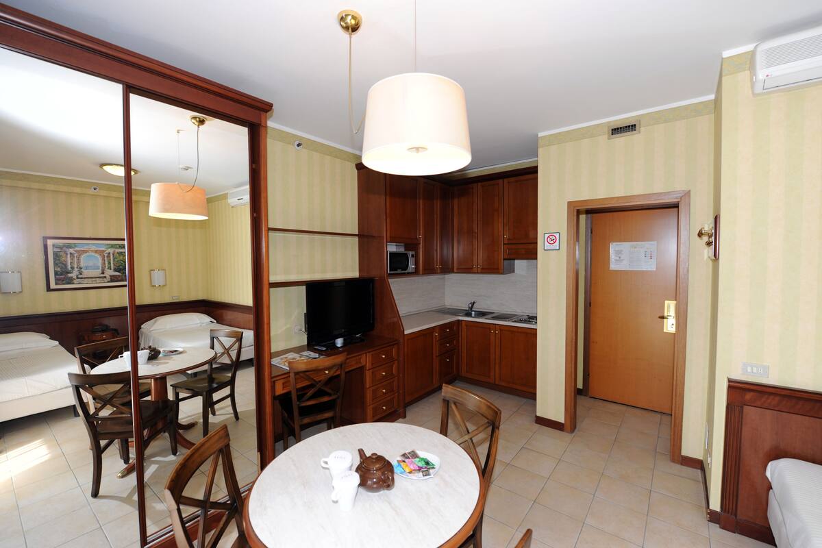 Una habitación de hotel compacta con comedor, kitchenette y una cama.