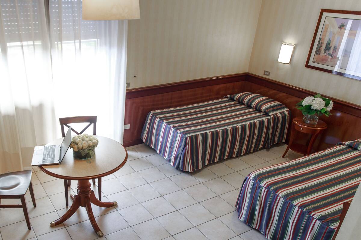Habitación de hotel con una mesa de comedor, dos camas individuales, un sofá y un ordenador portátil sobre la mesa.