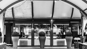 A covered waiting area with a modern design, featuring a central seating area with two planters and a glass storefront in the background. - Ripamonti Residence & Hotel (Pieve Emanuele)