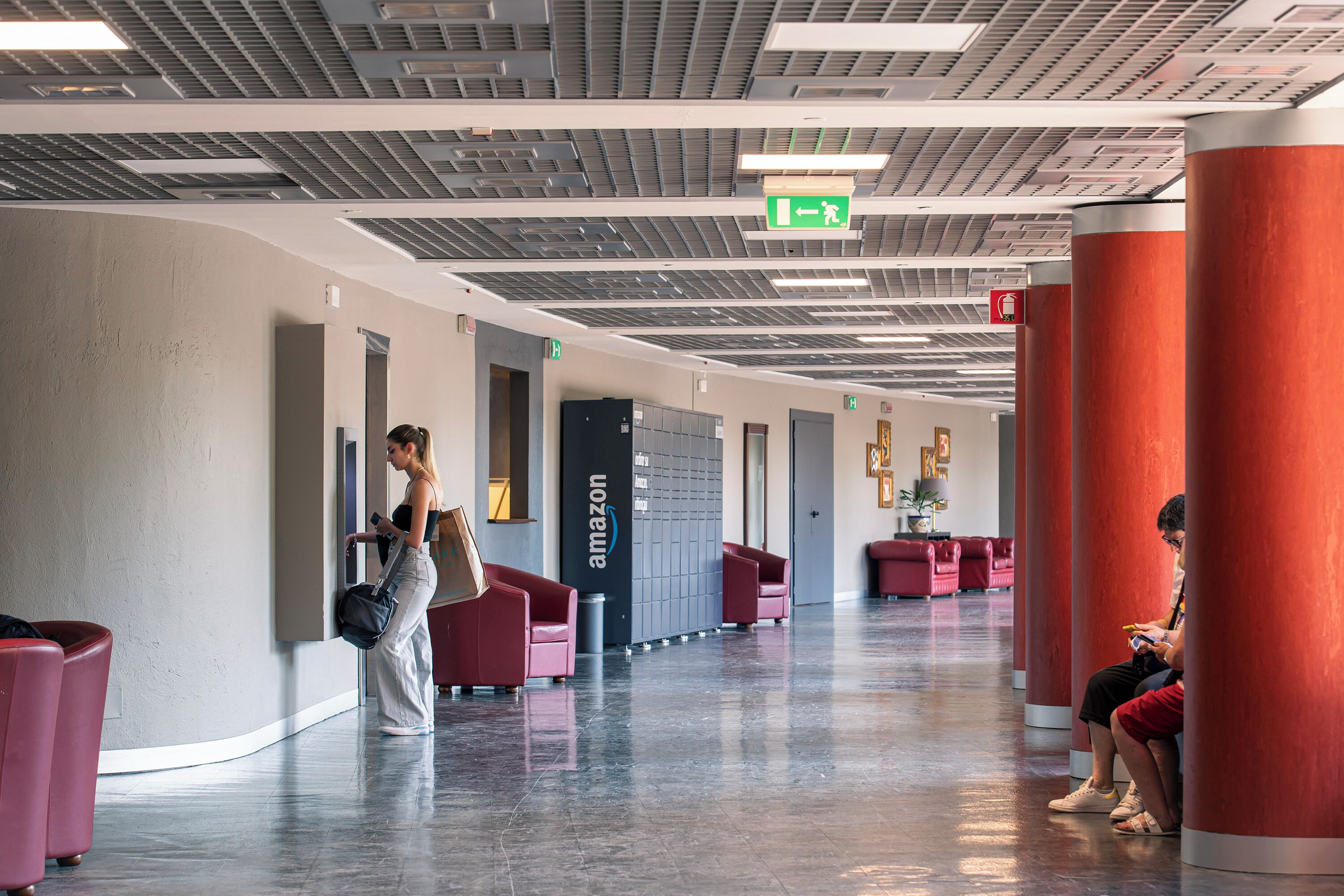 Um hall espaçoso com design moderno, apresentando um longo corredor com áreas de estar em vermelho e cinza e o logotipo da Amazon em destaque na parede.