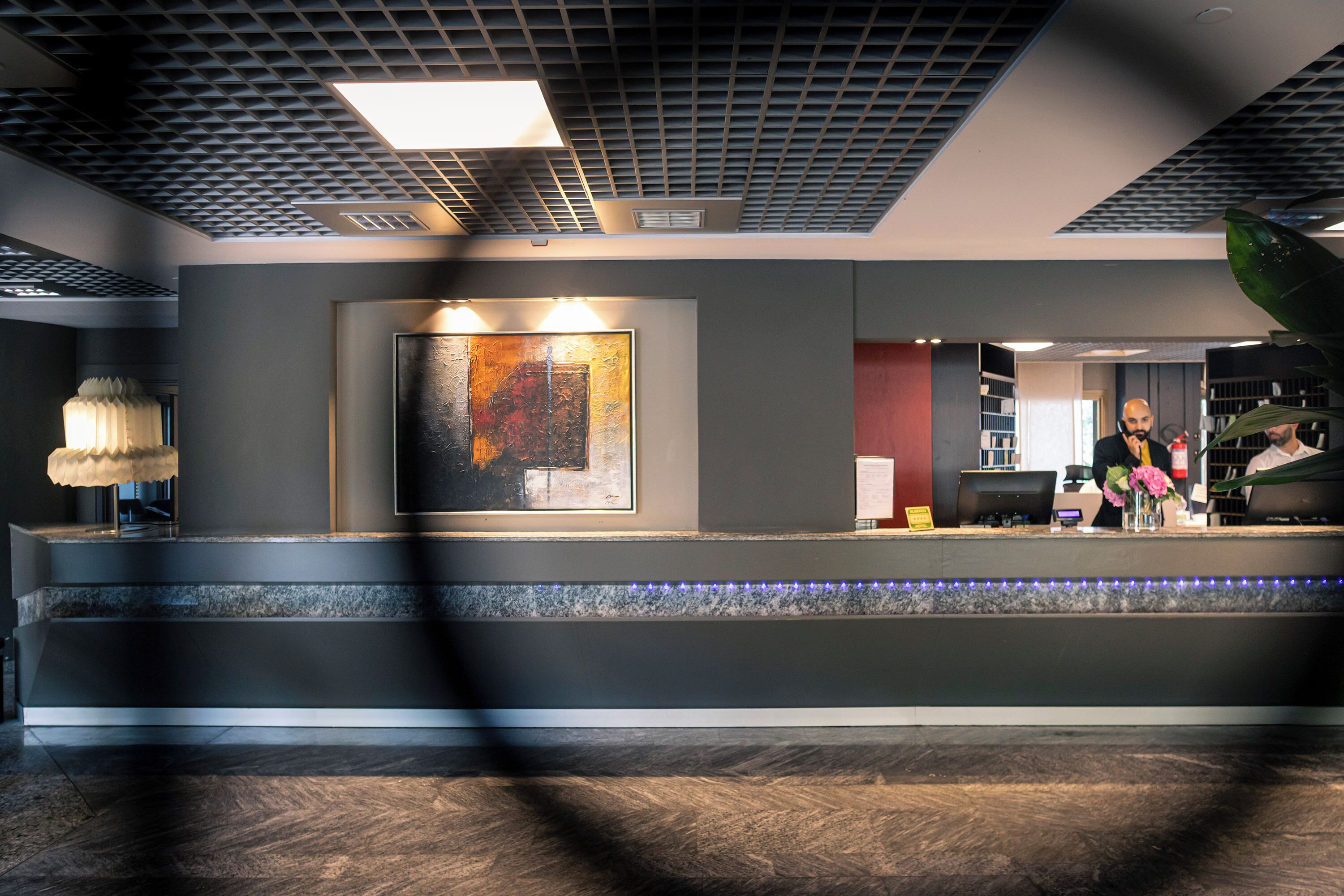 A modern reception area with a large abstract painting, a reception desk, and a staircase leading to an upper level.