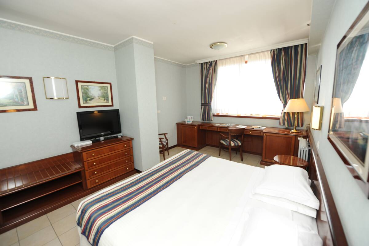 Habitación de hotel con cama, escritorio con silla, televisor y ventana con cortinas.