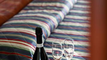 A bed with a colorful striped bedspread, a bottle of wine, and two empty wine glasses on a wooden table.