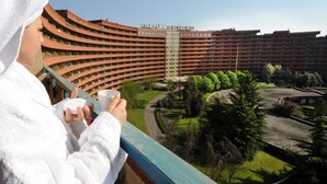 A person in a white robe holding a cup, overlooking a large, multi-story building with balconies and a central entrance. - Ripamonti Residence & Hotel (Pieve Emanuele)