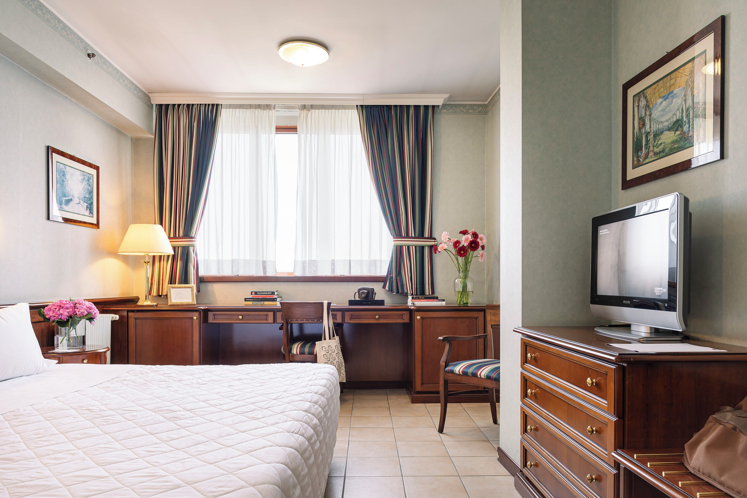 A hotel room with a bed, desk, chair, television, and a window with curtains.