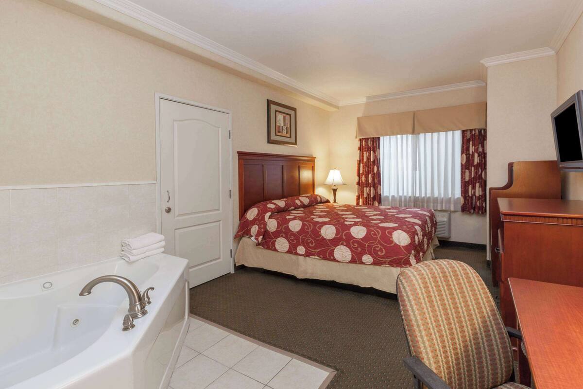 Ein Hotelzimmer mit einer großen Badewanne, einem Bett mit Blumendecke, einem Schreibtisch mit Fernseher und einem Fenster mit Vorhängen.