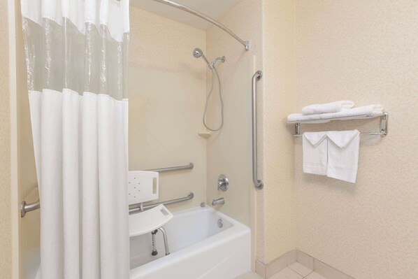 A bathroom with a bathtub, shower, grab bars, a towel rack, and a small sink. - Howard Johnson by Wyndham Bakersfield (Bakersfield)