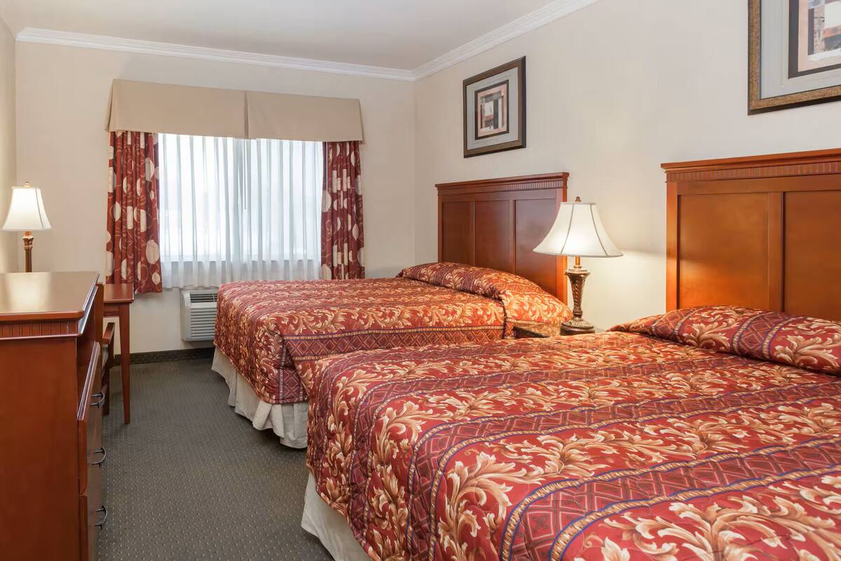 Ein Hotelzimmer mit zwei Betten, einem Schreibtisch, einer Lampe und einem Fenster mit Vorhängen.