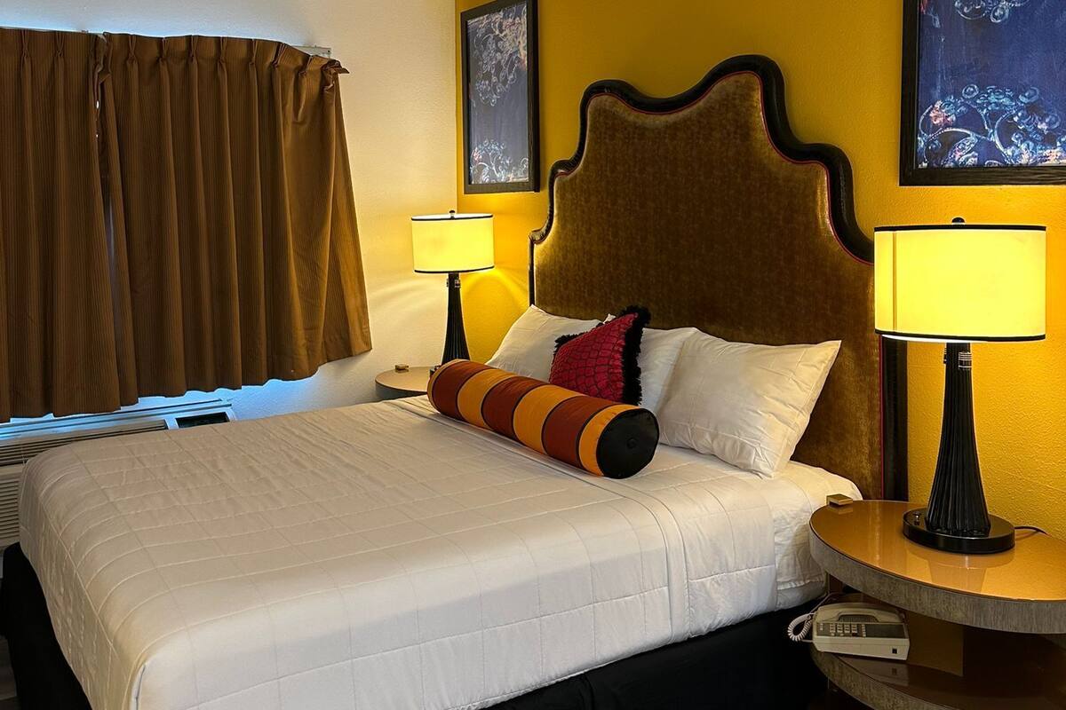 Ein Hotelzimmer mit einem großen Bett, zwei Nachttischen mit Lampen, einem Kopfteil und zwei gerahmten Bildern an der Wand.