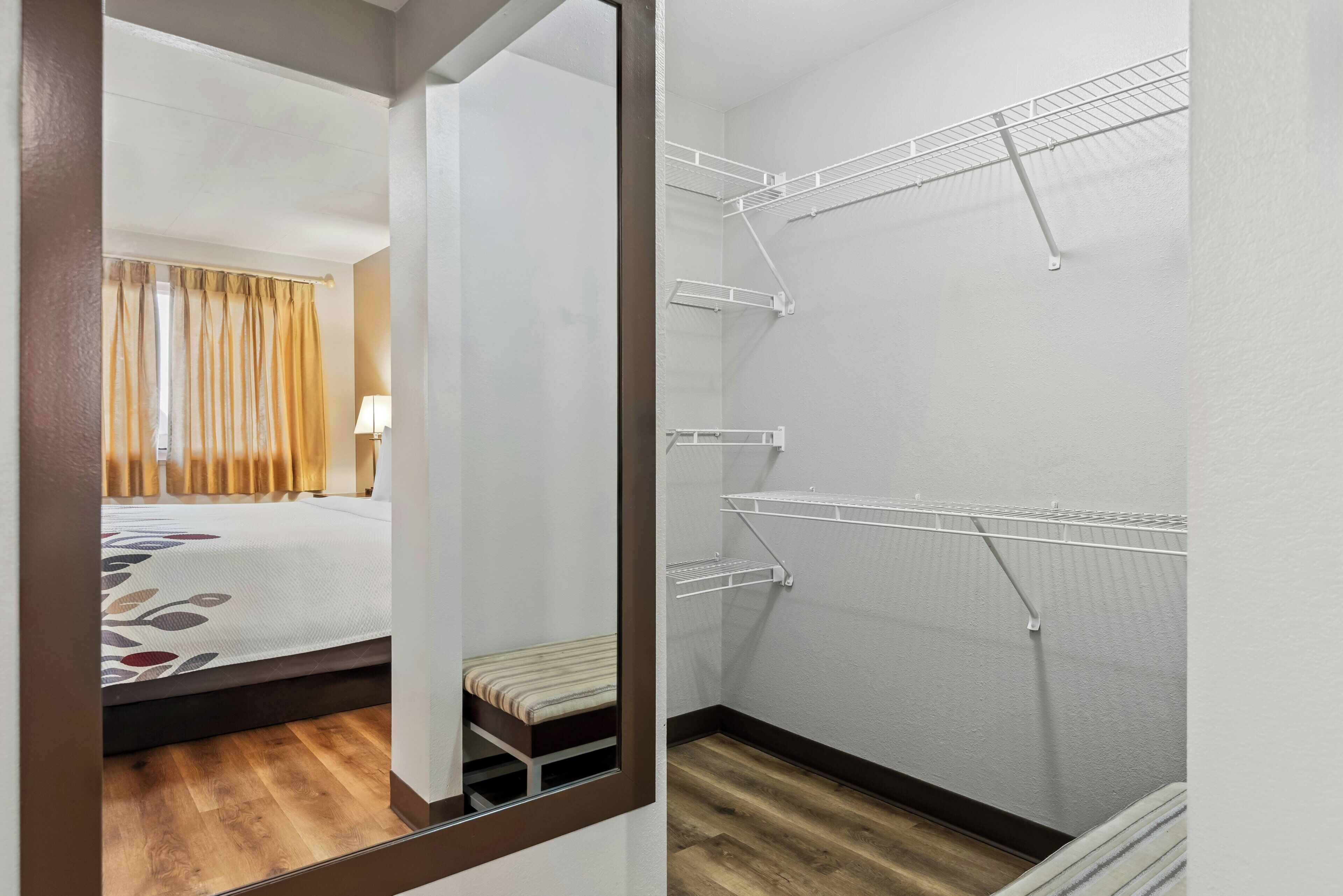 A hotel room with a bed, a bench, and a walk-in closet with shelves.
