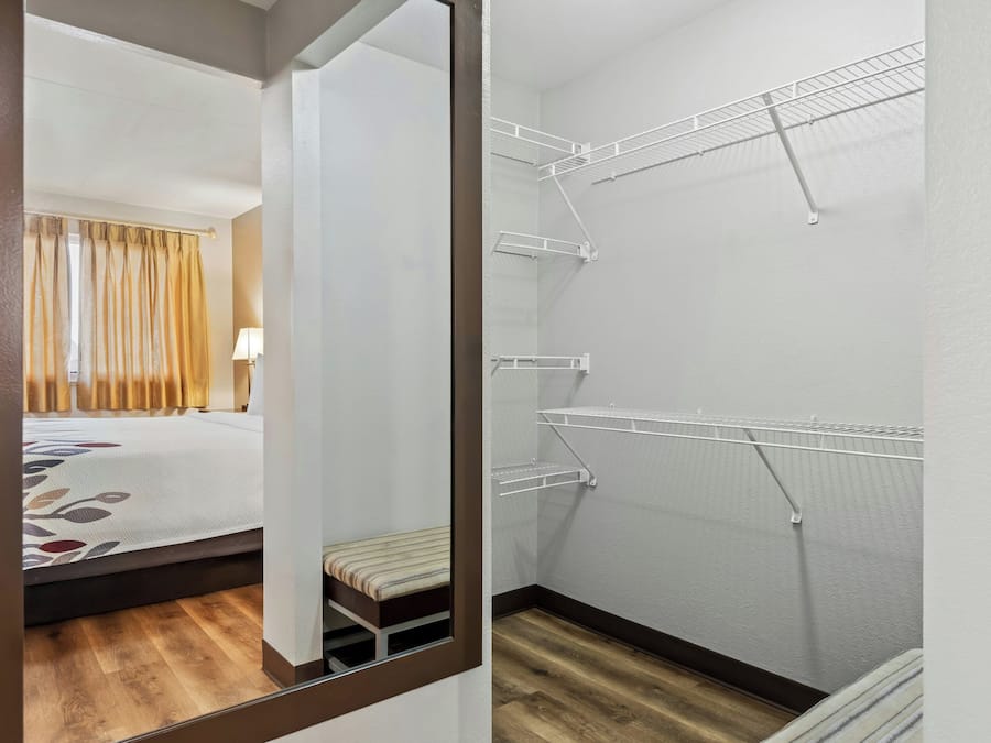 A hotel room with a bed, a bench, and a walk-in closet with shelves.